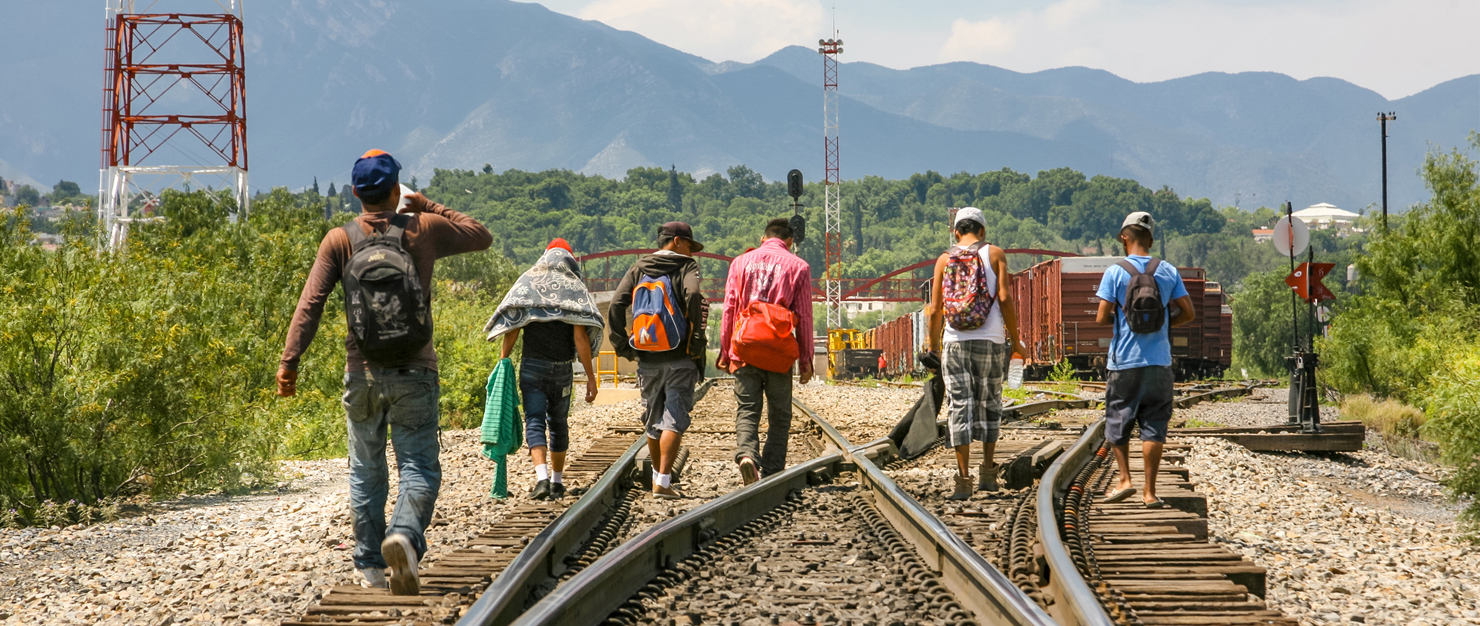 A group of Central American people walking along train tracks during their journey
