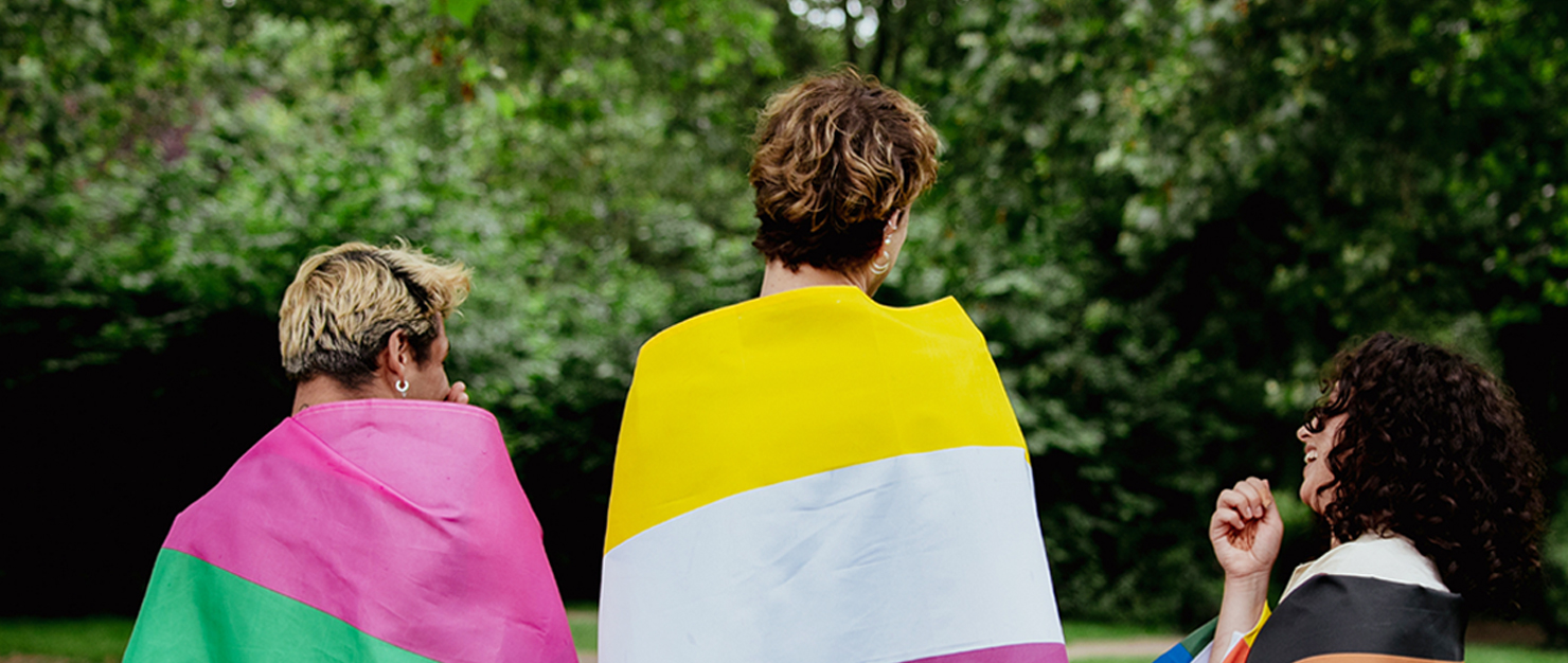 Three people wearing pride flags over their shoulders reflecting a diversity of LGBTQ+ identities 