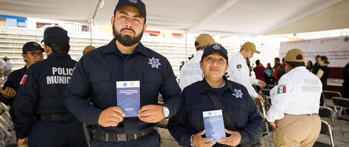 Two Oaxaca police officers hold up manuals on criminal investigation developed by WJP Mexico